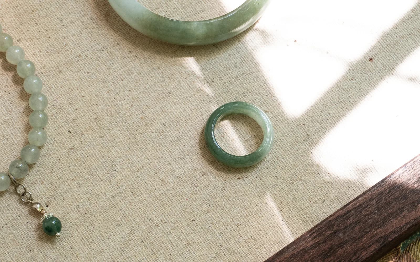 Vòng, nhẫn và chuỗi ngọc phỉ thúy trên khay linen dưới ánh nắng tự nhiên